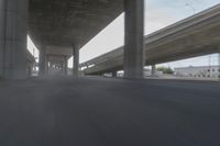 a view looking at the underside of an overpass, driving through a city street