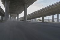 a view looking at the underside of an overpass, driving through a city street