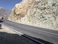 the car is driving along a winding mountain road next to rocks and a large rock wall