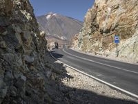 the car is driving along a winding mountain road next to rocks and a large rock wall