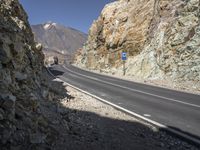 the car is driving along a winding mountain road next to rocks and a large rock wall