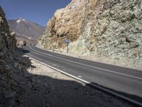 the car is driving along a winding mountain road next to rocks and a large rock wall