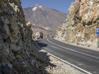 the car is driving along a winding mountain road next to rocks and a large rock wall