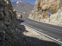 the car is driving along a winding mountain road next to rocks and a large rock wall