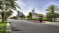 the road is lined with grass and tall buildings in the background of the picture, as well as palm trees