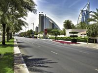 the road is lined with grass and tall buildings in the background of the picture, as well as palm trees