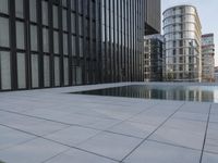 an empty parking lot that has black tiles on the ground and black windows reflecting the sky