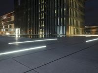 several light strips run along the sidewalk with buildings in the background at night time in the city