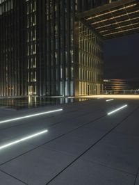 several light strips run along the sidewalk with buildings in the background at night time in the city