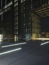 several light strips run along the sidewalk with buildings in the background at night time in the city