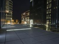 several light strips run along the sidewalk with buildings in the background at night time in the city