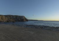 a beach at dusk with birds flying by the coast and people on the path at the shore