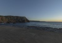 a beach at dusk with birds flying by the coast and people on the path at the shore