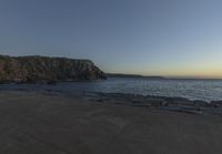 a beach at dusk with birds flying by the coast and people on the path at the shore