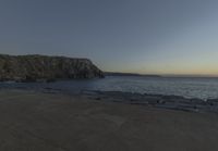 a beach at dusk with birds flying by the coast and people on the path at the shore