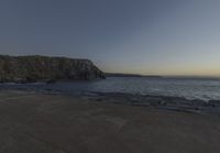 a beach at dusk with birds flying by the coast and people on the path at the shore