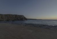 a beach at dusk with birds flying by the coast and people on the path at the shore