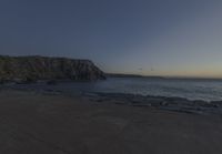 a beach at dusk with birds flying by the coast and people on the path at the shore