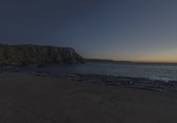 a beach at dusk with birds flying by the coast and people on the path at the shore