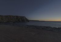 a beach at dusk with birds flying by the coast and people on the path at the shore