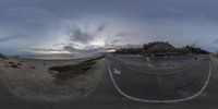 some clouds and the ocean near a beach and some cars on the road at dusk