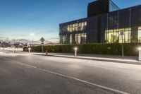 an empty city street at dusk with cars parked on it and building in the background