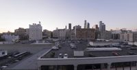 vehicles are seen parked in an empty parking lot at dusk, surrounded by large tall buildings