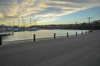 a person is walking near the water by boats and buildings on a river bank at dusk