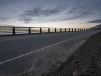 a truck driving past a wooden fence on the side of the road at dusk over a body of water