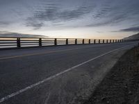 a truck driving past a wooden fence on the side of the road at dusk over a body of water