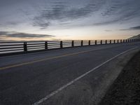 a truck driving past a wooden fence on the side of the road at dusk over a body of water