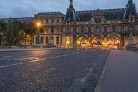 a street and the sky at dusk near a large building with an arch in front