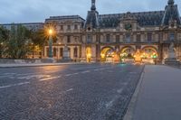 a street and the sky at dusk near a large building with an arch in front