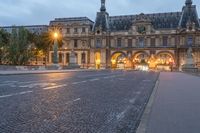 a street and the sky at dusk near a large building with an arch in front