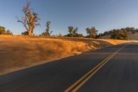 a car riding along a hill on the road near a dry grass field at dusk