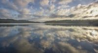 clouds moving over the calm waters at dusk near trees and hills on a foggy day