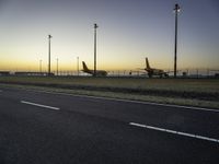 two planes are parked in the background on an open plain at dusk by street lamps