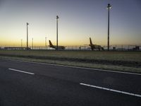 two planes are parked in the background on an open plain at dusk by street lamps