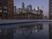 a puddle on a road is reflecting some buildings in the water at dusk by buildings