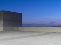 an empty parking lot next to tall buildings in a city at dusk with the moon shining brightly behind it