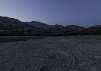 the ground is littered with rocks and stones at dusk with mountains in the distance and dark blue sky