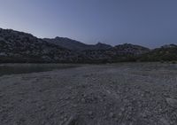 the ground is littered with rocks and stones at dusk with mountains in the distance and dark blue sky