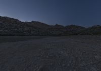 the ground is littered with rocks and stones at dusk with mountains in the distance and dark blue sky