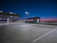 a parking lot lit up at dusk with light poles on the roof and other things on the ground