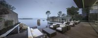 outdoor area of a resort with the pool at dusk in a modern location with wooden tables and white chairs