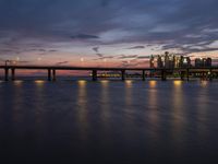 a long bridge spanning across a large body of water at dusk with lights shining on the side