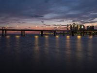 a long bridge spanning across a large body of water at dusk with lights shining on the side