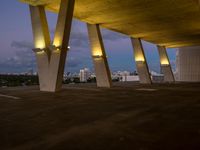 a view of the sky from the roof of an open area with concrete pillars at dusk