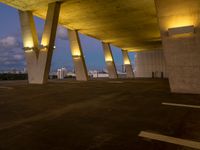 a view of the sky from the roof of an open area with concrete pillars at dusk