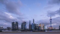 the skyline is lit up at dusk near the water and buildings with a long line of people waiting